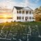 A house sits on a grassy lawn, with a blueprint displayed, highlighting the design and structure of the home.